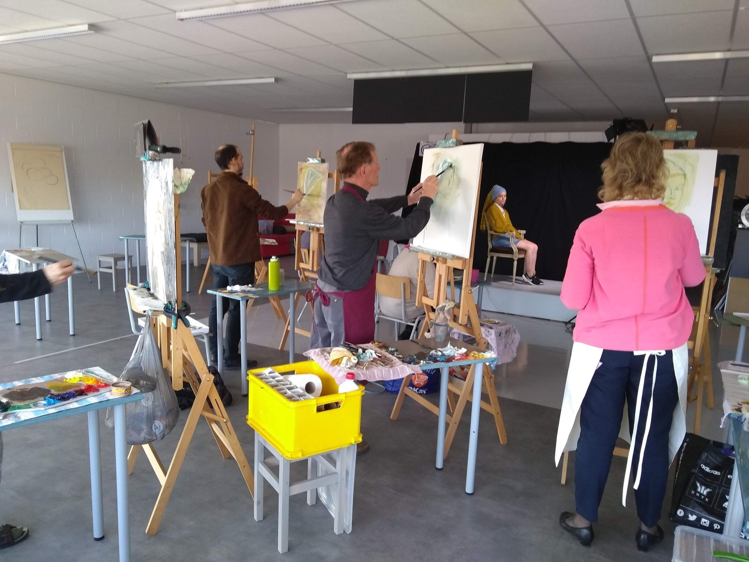 Meerdere mensen staan aan hun schildersezel en schilderen een levend model